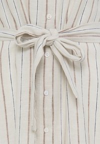 Bež tkanina z navpičnimi črtami, ozkimi rjavimi in črnimi črtami, belimi gumbi po sredini in tkanim trakom, vezanim okoli pasu.