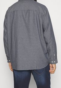 Camicia a maniche lunghe blu e bianca a fantasia, con polsini a bottone e colletto classico. Taglio dritto con tessuto testurizzato.