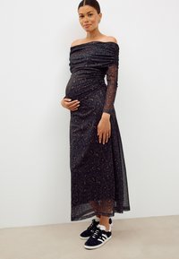 Robe noire à épaules dénudées avec imprimé léopard et détails froncés ; manches longues transparentes. Assortie à des baskets noires et blanches.