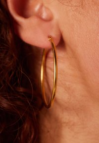Gouden oorring met een gladde, gepolijste oppervlakte, hangend aan een oorlel, met een eenvoudig, circulair ontwerp.