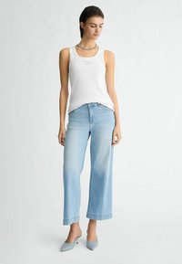 Débardeur blanc côtelé avec un col rond, assorti à un jean large bleu clair et à des talons bleu clair avec des embellissements. Tenue simple et décontractée.