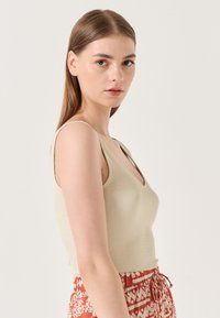 Débardeur beige à côtes avec un décolleté en V profond et des bretelles fines, associé à un pantalon taille haute à motifs rougeâtre et brun.