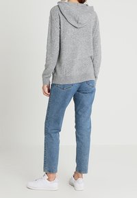 Pull à capuche gris avec poignets et ourlet côtelés, associé à un jean droit bleu et des baskets blanches, vu de dos.