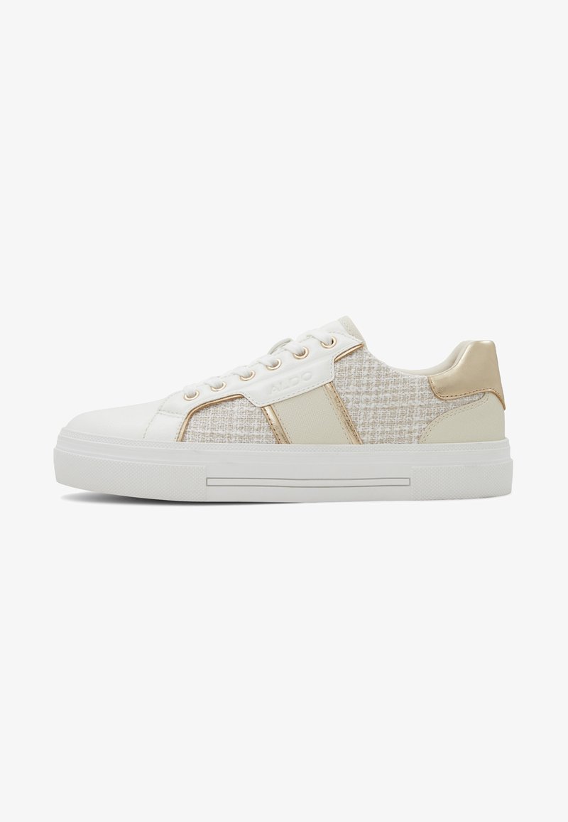 Baskets basses avec semelle blanche, côtés en tissu tweed beige, lacets blancs et détails métalliques dorés sur le talon et les œillets.