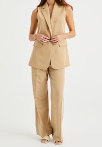 Beige skräddarsydd väst och byxset, ärmlös design, modern slag, två framfickor, mjukt tyg, flödande silhuett, minimala hårdvaruaccenter.