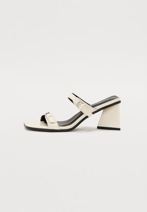 Off-white heeled sandals with two thin straps, a square toe, and a geometric, block heel. Smooth leather finish with black accents.