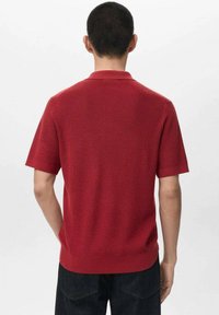 Rød polo med korte ærmer og ribbet struktur samt krave. Har en lige kant og en afslappet pasform, fremstillet af blødt strikket materiale.
