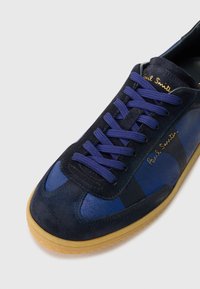 Baskets en daim bleu marine avec des accents bleu clair. Présentent des lacets plats violets et une semelle en caoutchouc. Marquage doré "Paul Smith" sur le côté.