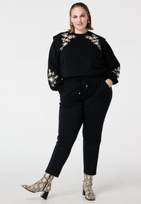 Zwarte sweatshirt met bloemenborduursel op de schouders en mouwen, gecombineerd met zwarte taps toelopende broek. Gecompleteerd met patroon enkellaarsjes.