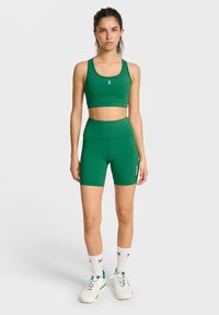 Grön träningsset som består av en åtsittande crop top och högmidjade shorts, tillverkade av ett slätt tyg med vit logodetalj på shortsen.
