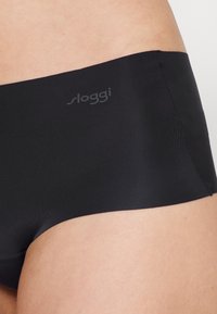 Black Sloggi hipster panties made of smooth, stretchy fabric. Features a seamless design and minimalistic branding on the waistband.