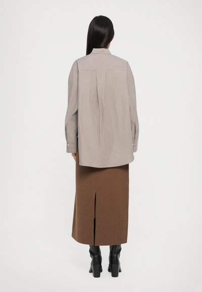 Long-sleeve striped shirt in beige and white, paired with a brown knee-length skirt featuring a side slit. Black heeled boots complete the look.