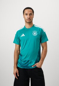 A camisola desportiva em azul-petróleo apresenta um decote redondo, detalhes em branco e o emblema nacional da Alemanha com quatro estrelas. Feita de tecido suave e leve.