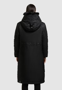 Garš melns pūkains mētelis ar kažokādas oderi. Iezīmēts ar sašaurinātu vidukli, mīkstu tekstūru un rāvējslēdzēju ar pogām aizmugurē.