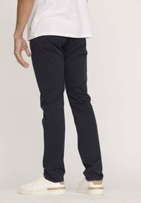 Pantalons slim bleu marine, en coton, avec une texture lisse et un design minimaliste. Associés à des baskets blanches.