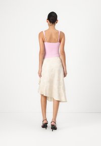 Roze aansluitend camisole met dunne bandjes, gecombineerd met een crèmekleurige asymmetrische rok met bloempatronen. Zwarte sandaaltjes met bandjes.