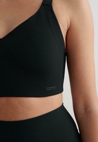 Černá žebrovaná sportovní podprsenka s nastavitelnými ramínky, na dolním okraji s logem. Materiál je měkký na dotek a má přiléhavý střih.