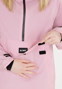 Rosa wasserdichte Jacke mit schwarzen Akzenten, ausgestattet mit einem Reißverschluss vorne, seitlicher Tasche mit Klettverschluss und einer weichen Textur.
