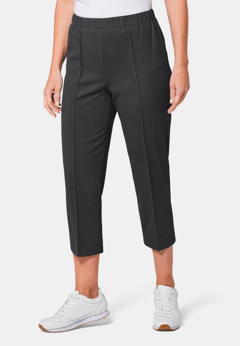 Schwarze, cropped Hosen aus strukturiertem Stoff mit gestepptem Design und elastischem Bund, kombiniert mit weißen Sportschuhen.