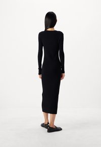 Svart ribbad trikåklänning med långa ärmar, åtsittande silhuett och längd till mitten av vaden. Matchad med platta svarta skor med sidodekorationer.