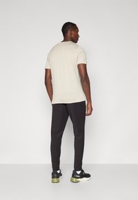 Beige korte mouwen shirt, zwarte taps toelopende broek, zwarte sneakers met groene accenten. Glad materiaal, relaxte pasvorm, minimalistisch ontwerp.