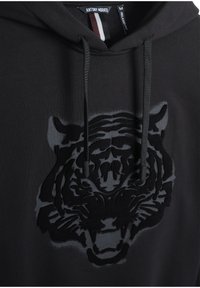 Felpa nera con cappuccio, decorata con una grafica in tessuto di testa di tigre nera opaca. Presenta un cappuccio con cordino e un tessuto morbido con una vestibilità comoda.