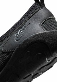 Κοντινό πλάνο της φτέρνας μαύρου αθλητικού παπουτσιού Nike με υφασμάτινο επάνω μέρος και ανάγλυφο λογότυπο Nike, με υφή στη σόλα.