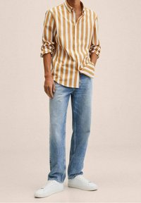 Camicia a maniche lunghe a righe gialla e bianca, abbinata a jeans a gamba dritta azzurri chiari e sneakers bianche. Vestibilità casual, design con bottoni.