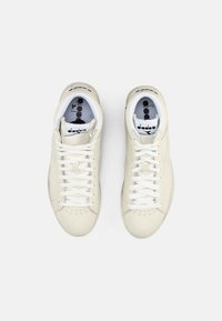 Cream-colored leather sneakers with white laces, perforated toe, and a padded collar. Branding on the tongue features black text and color accents.