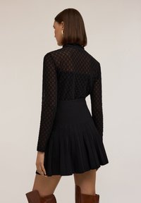 Černé šaty s dlouhými rukávy, průhledným vzorovaným vrškem, pevným pasem a plisovanou sukní. Nošeno s hnědými kozačkami do kolen.