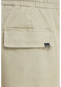 Light beige shorts made of cotton with an elastic waistband. Features a back pocket with a flap and a small black tag displaying "ISOLID."