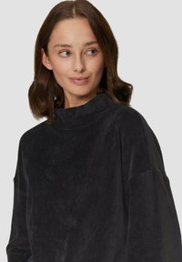 Must mustre pullover kõrge kaelusega, ribakujunduse ja langenud õmblustega. Pehme kangas ja lõdva istuvuse kujundus tagavad mugavuse.