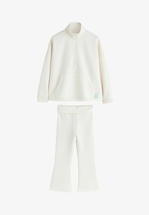 Balta vilnos megztinis su pusiau užtrauktuku ir aukštu kaklu, priekyje kišenė; atitinkamos spalvos platėjantys kelnės su elastinga liemens juosta.