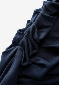 Tissu bleu marine foncé, drapé doucement avec une texture et des plis visibles. Le matériau semble tricoté avec une surface lisse et légèrement brillante.