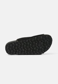 Scarpa nera slip-on con suola in gomma testurizzata a motivo circolare e tomaia in suede con dettagli dorati sulla fascia.