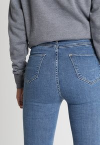 Modré džíny s vysokým pasem, přiléhavého střihu, s dvěma zadními kapsami, jemným opotřebením a směsí bavlny pro pohodlí.