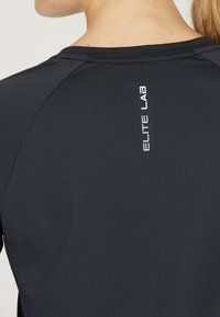 Mustan urheilupaidanka kangas on tekstuurilla, ja siinä on pyöreä kaula-aukko sekä pieni valkoinen "ELITE LAB" -logo takana.