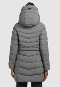 Woman wearing a long gray padded coat with a large hood, shown from the back against a plain background.