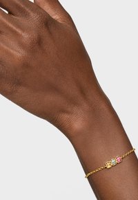 Złota bransoletka łańcuchowa z trzema kolorowymi zawieszkami w kształcie kwiatów: jasnoniebieską, różową i żółtą. Gładka faktura metalu, delikatny design.