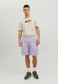 Beige short-sleeve t-shirt with graphic detail; light purple shorts with elastic waist; gray athletic shoes; white socks. Simple design.