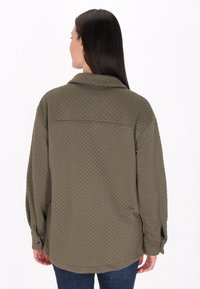 Camicia trapuntata verde oliva con colletto, dotata di maniche lunghe e polsini con bottoni. Tessuto liscio con un motivo a rombi.