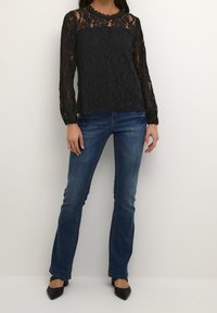 Svart spets långärmad topp med hög hals och scalloped trim, ihop med blå denimjeans och svarta spetsiga klackar.