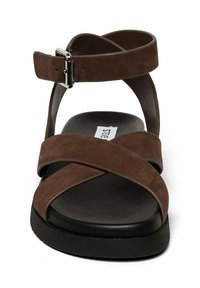 Sandale en suede marron avec des brides entrecroisées, une sangle à la cheville, une boucle carrée et une semelle texturée noire. Design simple, style à bout ouvert.