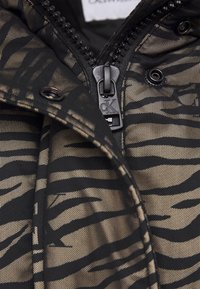 Czarna i brązowa kurtka z zebrą i zamkiem błyskawicznym, wykonana z teksturowanej tkaniny, z wyraźnym uchwytem suwaka z detalem logo oraz zatrzaskami.