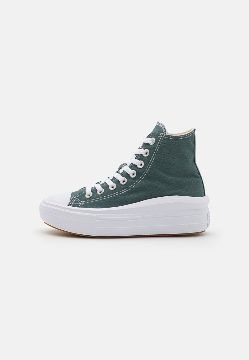 Adidași cu vârf înalt, din pânză verde, cu șireturi albe, vârf proeminent și o talpă groasă albă, cu un fond texturat maro.