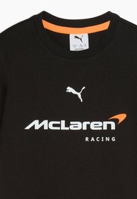 Schwarzes McLaren Racing T-Shirt mit weißem Puma-Logo und orangefarbenem Akzent im Kragen, Größenetikett am Hals sichtbar.