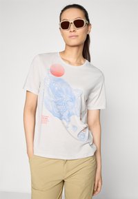 Ljusgrå t-shirt med blå topografiska linjer, röd cirkelgrafik och textinslag, tillverkad av mjukt bomullstyg, rund halsdesign.