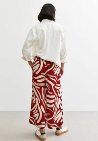 Loose-fitting cream shirt with rolled sleeves, paired with wide-leg red pants featuring a white abstract pattern. Simple white sneakers.