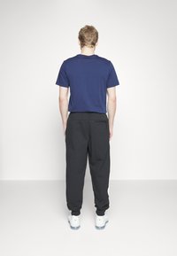 Camiseta de manga corta azul marino combinada con pantalones negros de corte suelto que tienen un bolsillo lateral, usados con zapatillas deportivas blancas y amarillas.