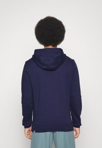 Felpa blu navy con cappuccio regolabile, polsini a costine e una piccola etichetta logo lungo l'orlo inferiore. Tessuto morbido e vestibilità comoda.